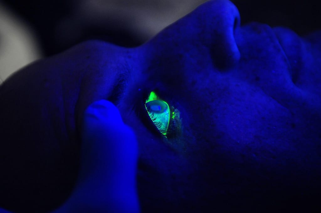 Close-up of a human eye glowing green under blue light, symbolizing the advanced technology and precision involved in the Future of Laser Vision Correction procedures.