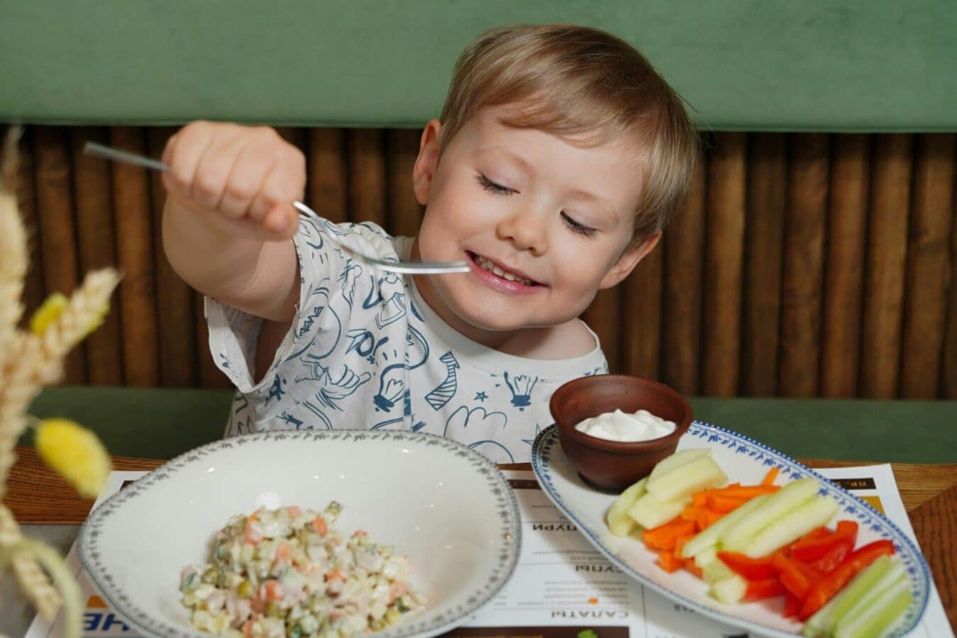 A smiling child enjoying a healthy meal rich in colorful vegetables and fish, representing nutrition for eye health.