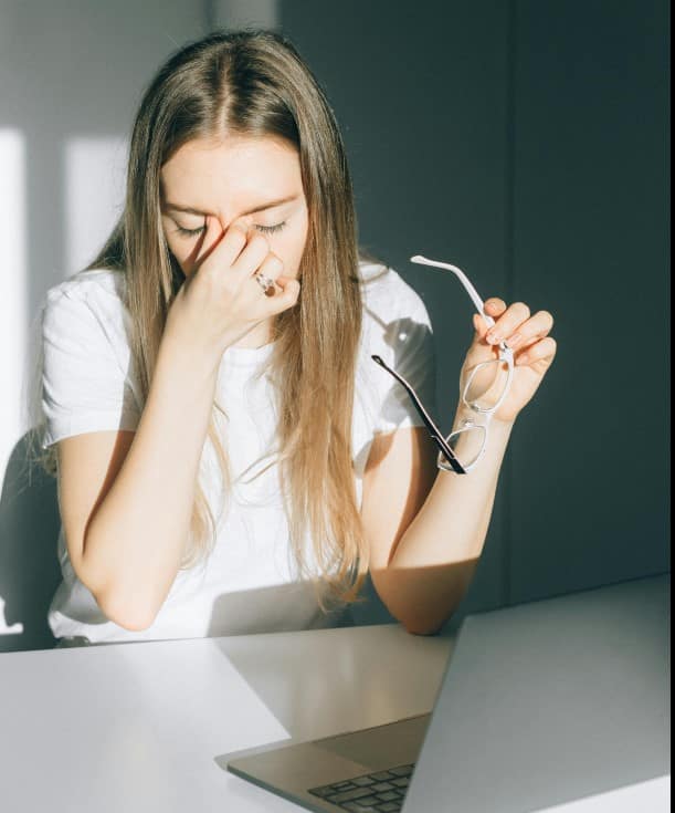A woman rubbing her eyes at her desk, showing common symptoms of digital eye fatigue